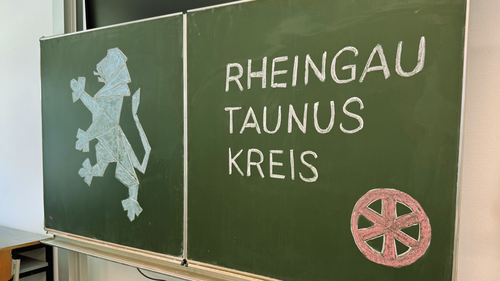 Zu sehen ist eine Schultafel im Klassenzimmer mit der in Kreide geschriebener Aufschrift "Rheingau-Taunus-Kreis".