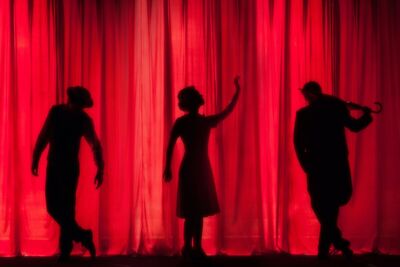 Silhouetten von drei Schauspielern vor rotem Bühnenvorhang.