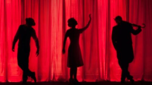 Silhouetten von drei Schauspielern vor rotem Bühnenvorhang.