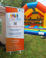 Foto: Zu sehen ist ein Roll-Up mit INfos zu den Frühen Hilfen, im Hintergrund eine Hüpfburg.
