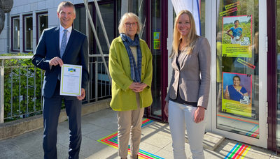 Foto v.l.n.r.: Landrat Frank Kilian, Fairtrade-Dezernentin Dorothee Nabrotzky, Fairtrade-Koordinatorin Eva Klos. Im Hintergrund zu sehen ist die Aktion zur Fashion Revolution, die auf fair gehandelte Textilien hinweist. 