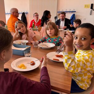 Kinder in der Schulmensa beim Mittagessen, im Hintergrund Pressevertreter und Landrat.