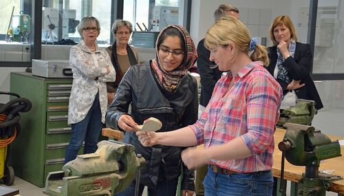 Aufgabe erfüllt: Der Fisch ist zu erkennen. Anja Braun begutachtet das Ergebnis der jungen geflüchteten Frau, die aus Afghanistan kam. Im Hintergrund sind (von links nach rechts) Beate Gottschall und Dr. Dorothee Freudenberg von der Stiftung CITOYEN sowie Schulleiter Markus Enders (verdeckt) und Daniela Leß zu sehen.