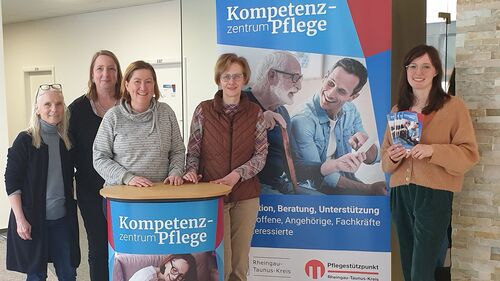 Bild: Das Team des Kompetenzzentrums Pflege des Rheingau-Taunus-Kreises steht vor einem Veranstaltungsplakat.