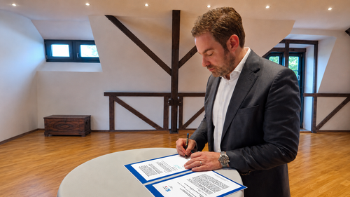 Landrat SAndro Zehner unterschreibt einen Brief am Tisch.